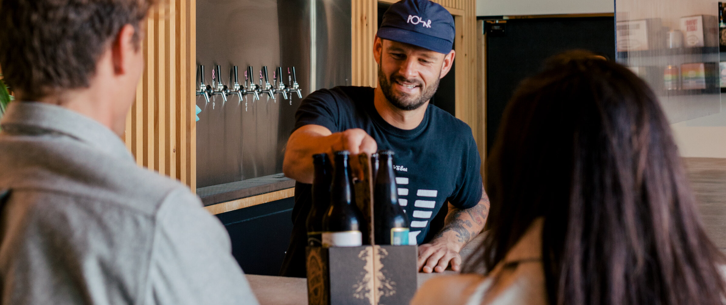 Person behind the bar at a brewery talking with customers and handing them beers.