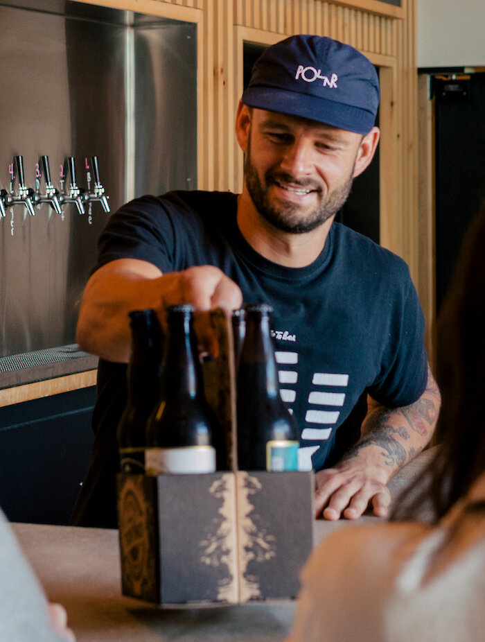 Person behind the bar at a brewery talking with customers and handing them beers.