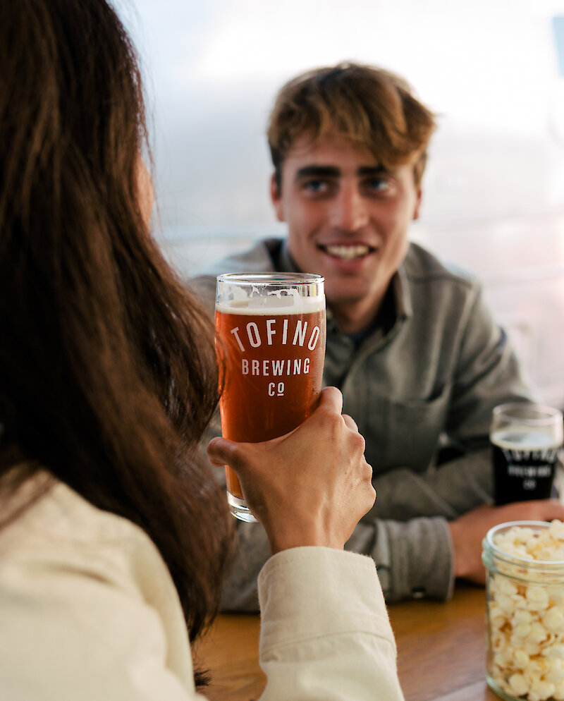 Person holding a Tofino Brewing pint of beer with a person smiling the background