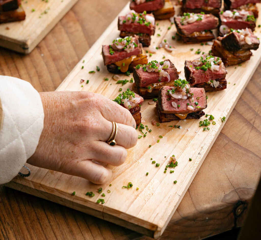 Person taking a steak appetizer from a board