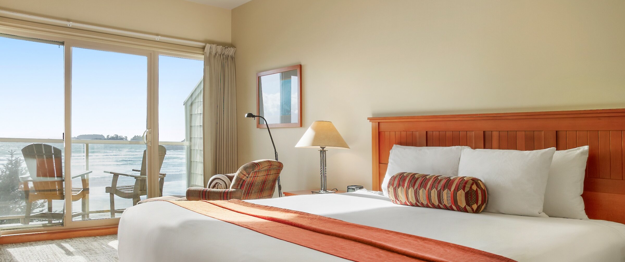 Hotel bedroom with bed and chair and a view of the ocean from the deck