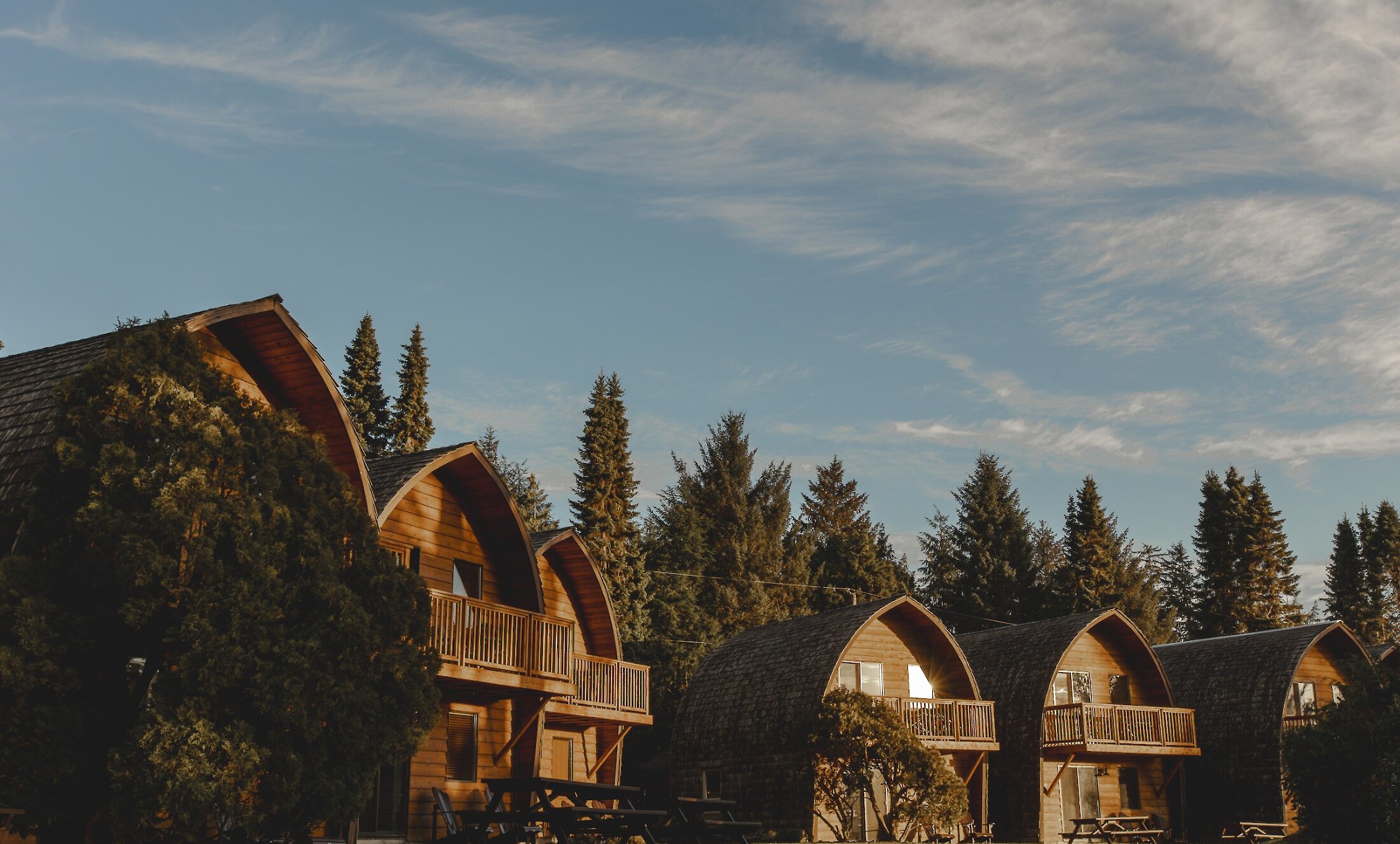 Wooden Quonset style huts with forest in background and blue sky