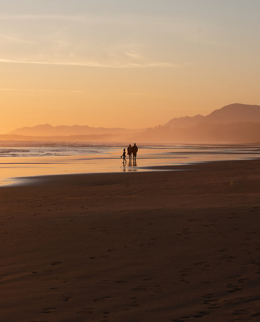 Two people and a child walking along Wickaninnish Beach at sunset