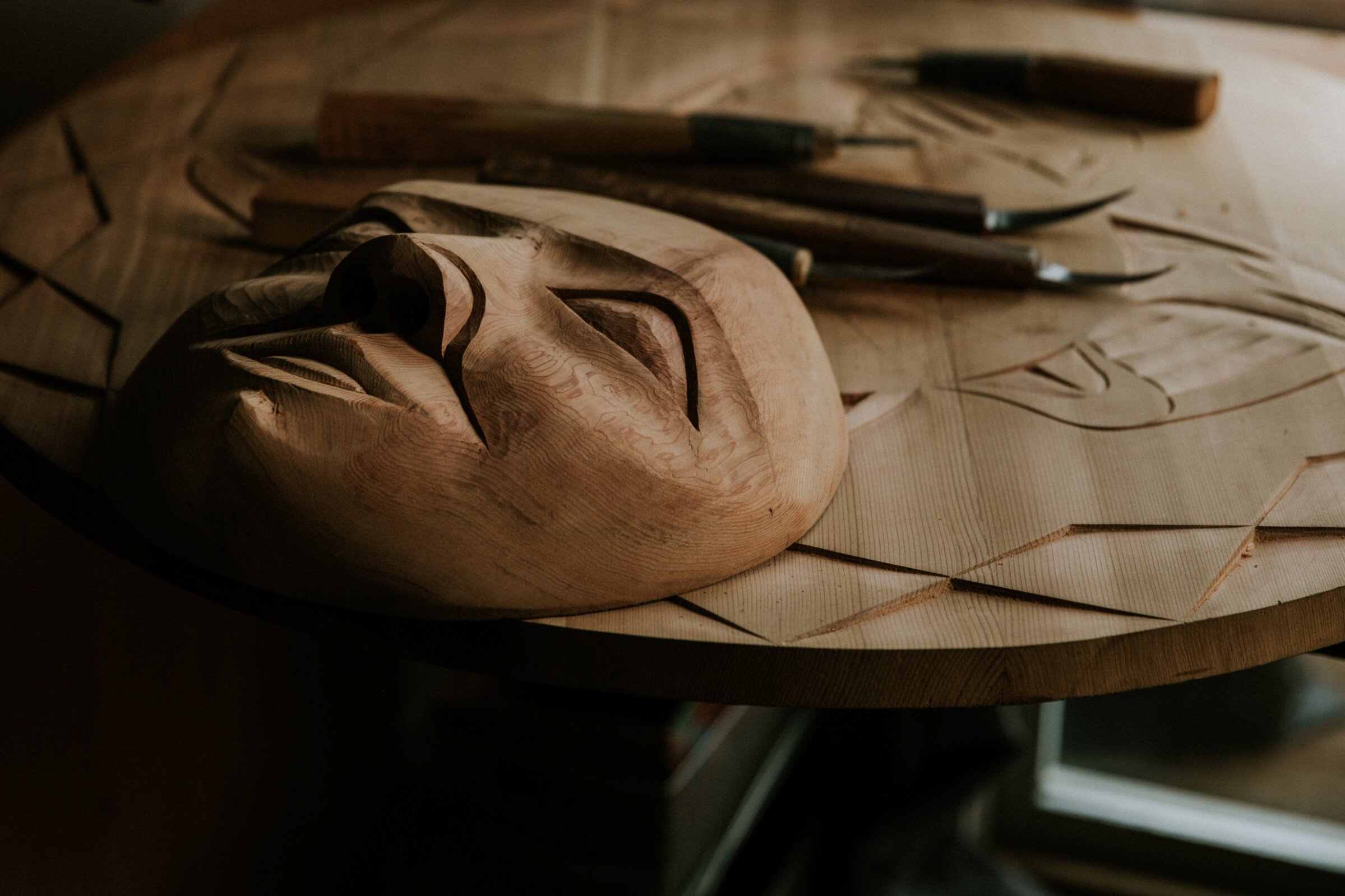 Wooden Indigenous carving of a face in progress with tools in the background