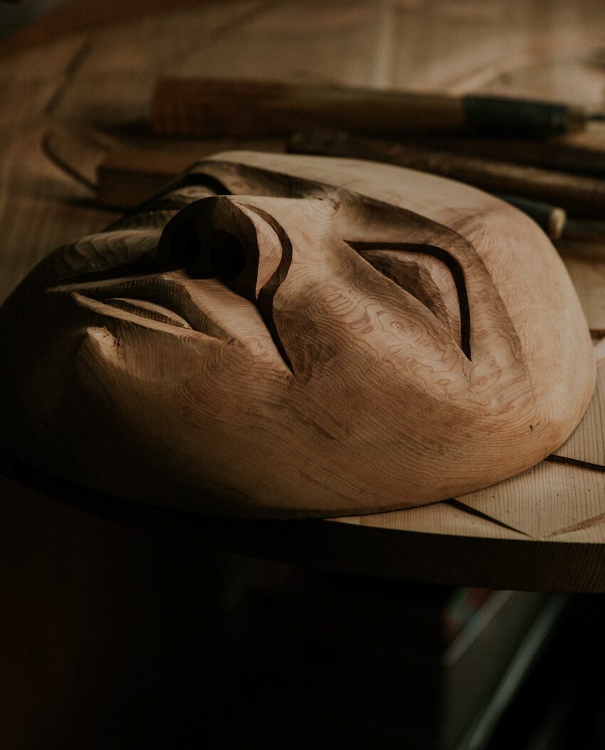 Wooden Indigenous carving of a face in progress with tools in the background