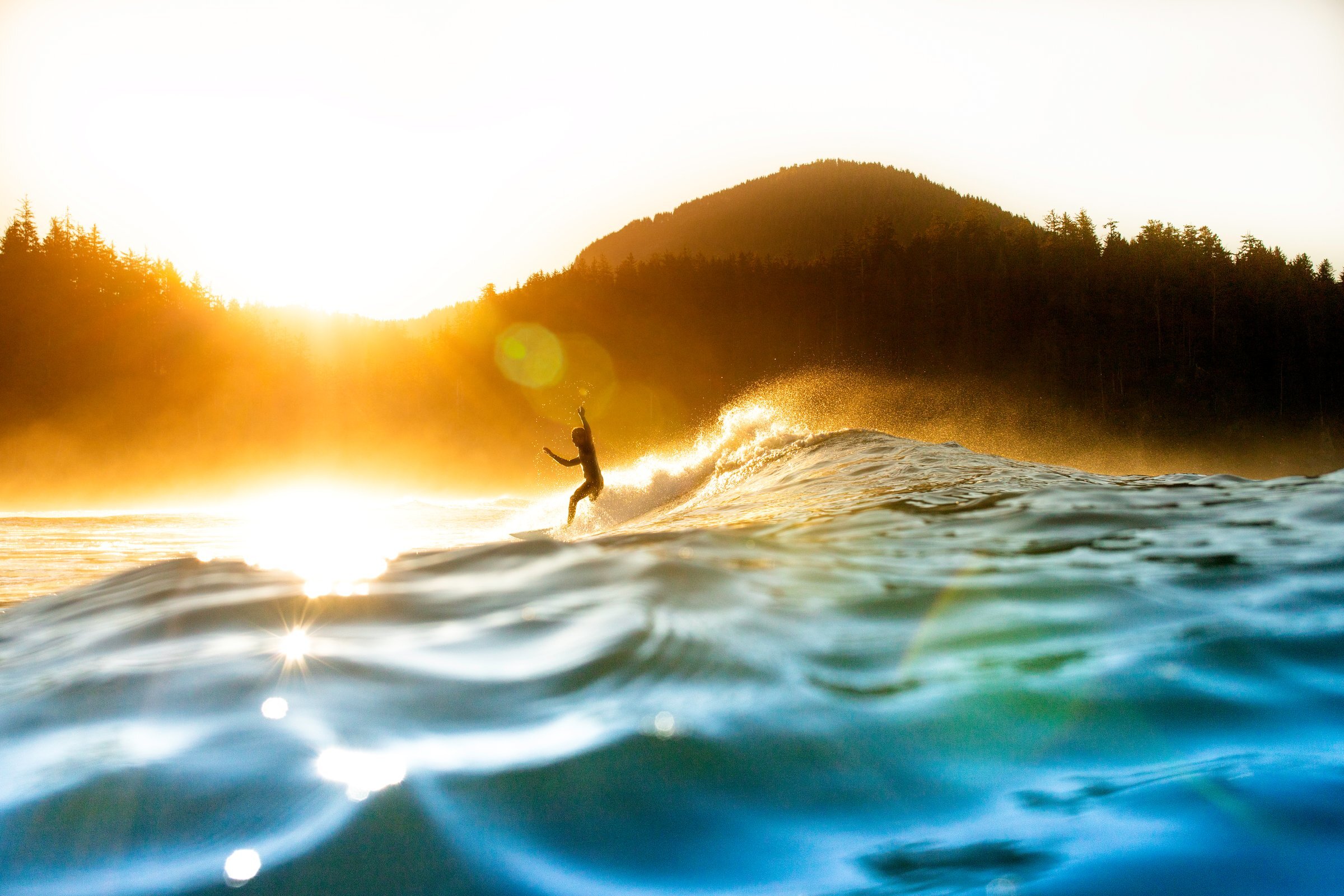 Sun glistening on the water with a surfer in the backgroun
