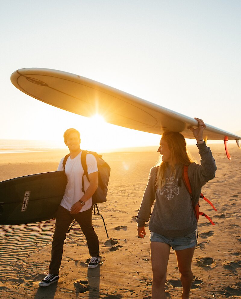 Two people walking on the beach carrying surfboards in the sunset