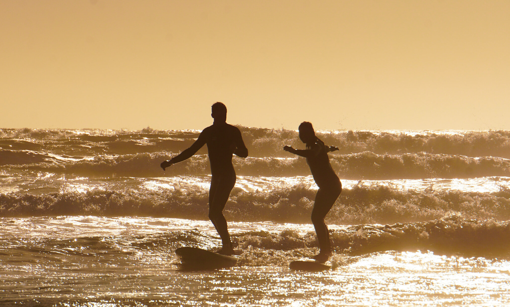Silhouettes of two people surfing during a golden sunset