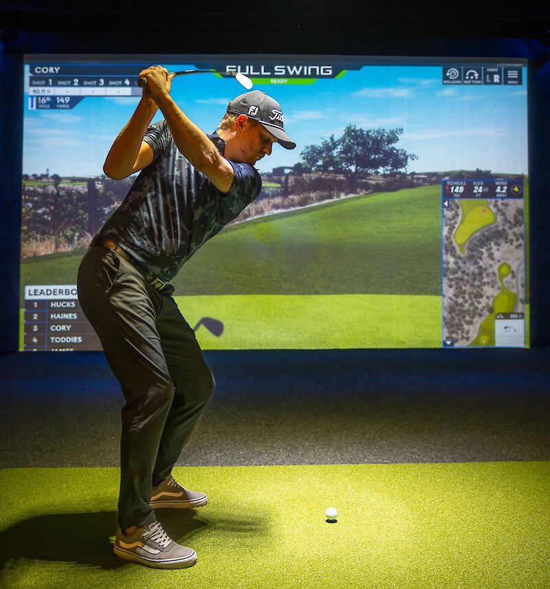 Person swinging in front of the indoor golf simulator at Long Beach Golf Course.