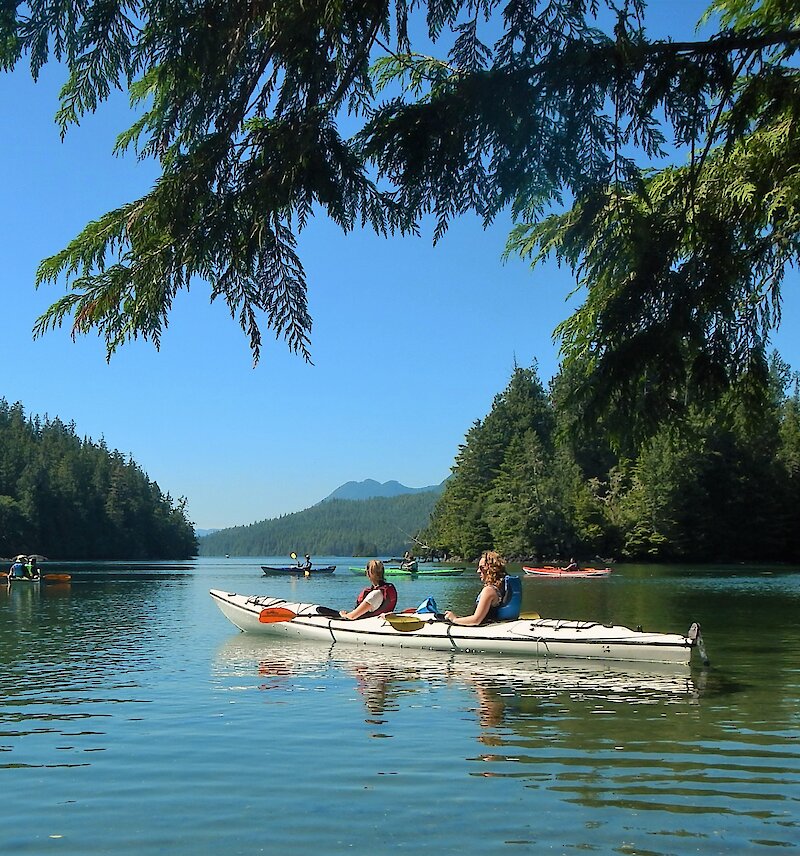 People in a tandem kayak in a calm inlet with other paddlers in the background