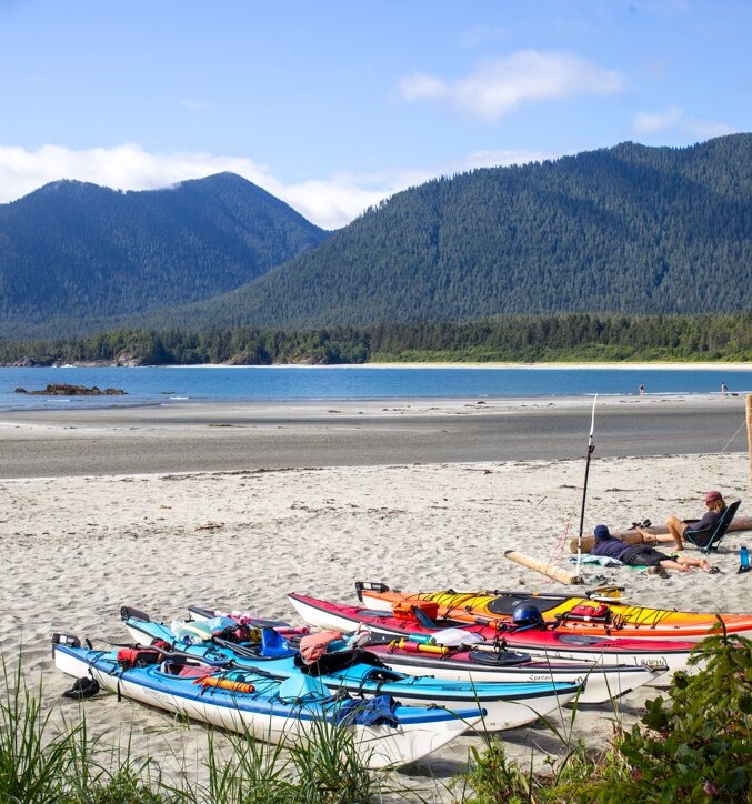Kayaks lined up on the beach at Cow Bay on Flores Island with people relaxing to the side of them