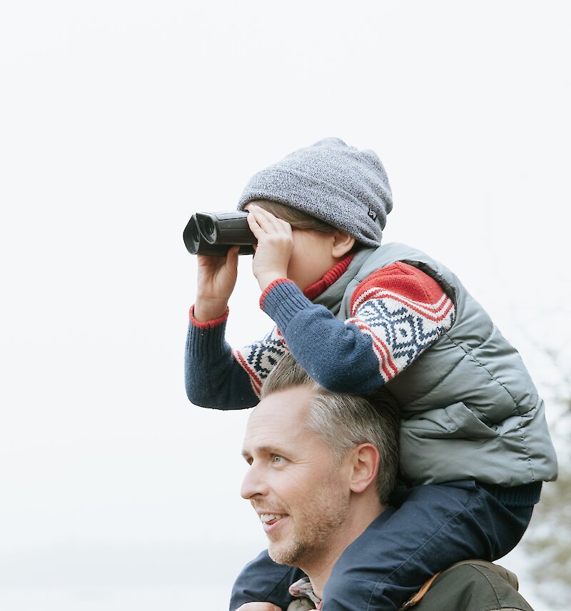 Father with child on his shoulders looking through binoculars