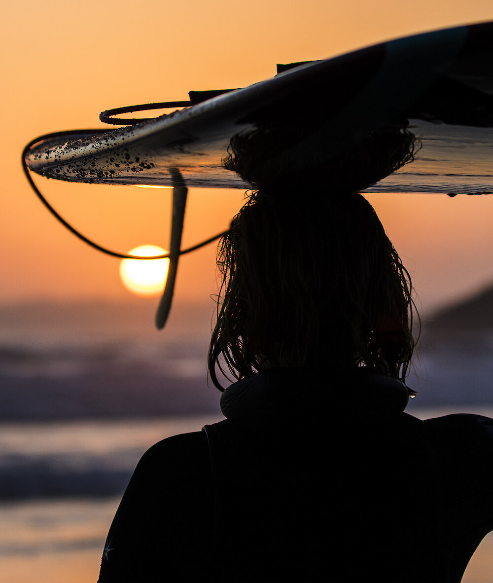 Person looking at the sunset with their surfboard resting on their head